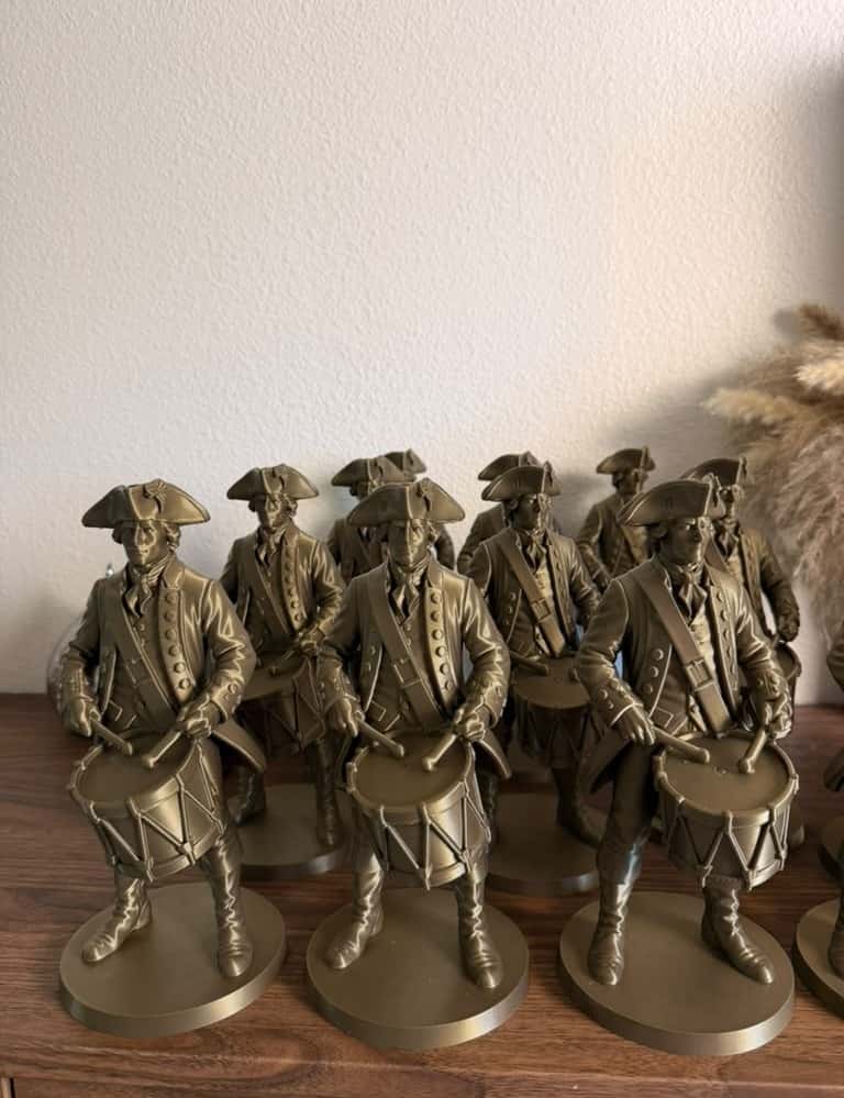Sixteen bronze Colonial Drummer figures lined up on a wooden sideboard